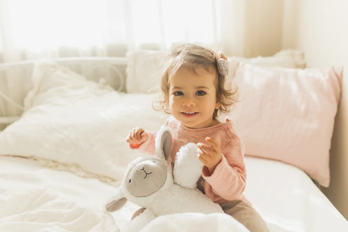 Toddler girl sitting up in bed with stuffed animal