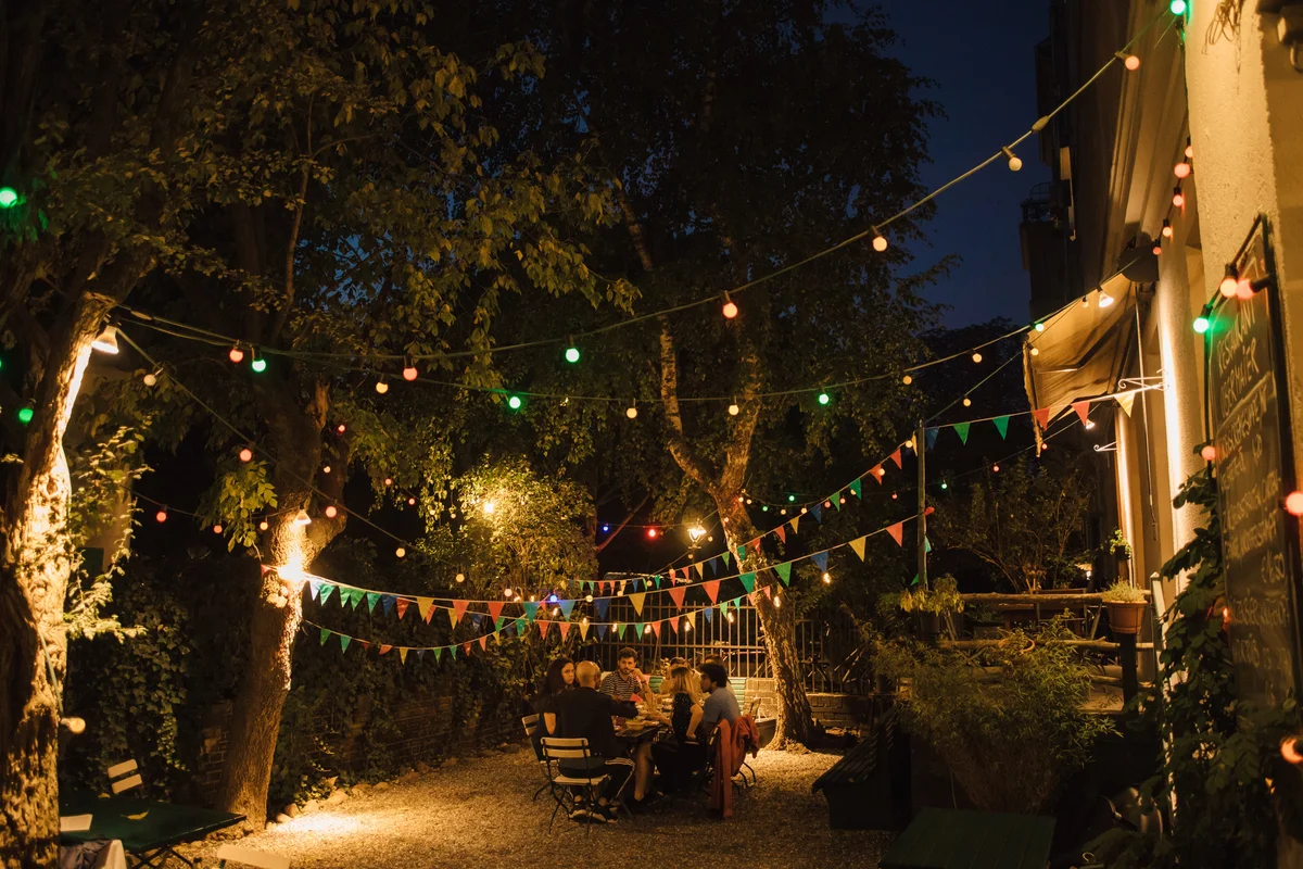 group of friends at table in backyard with colorful lights hanging above them