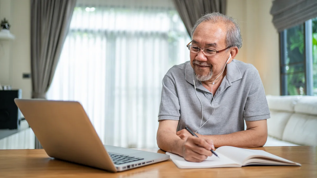 older man learning on his laptop and taking notes