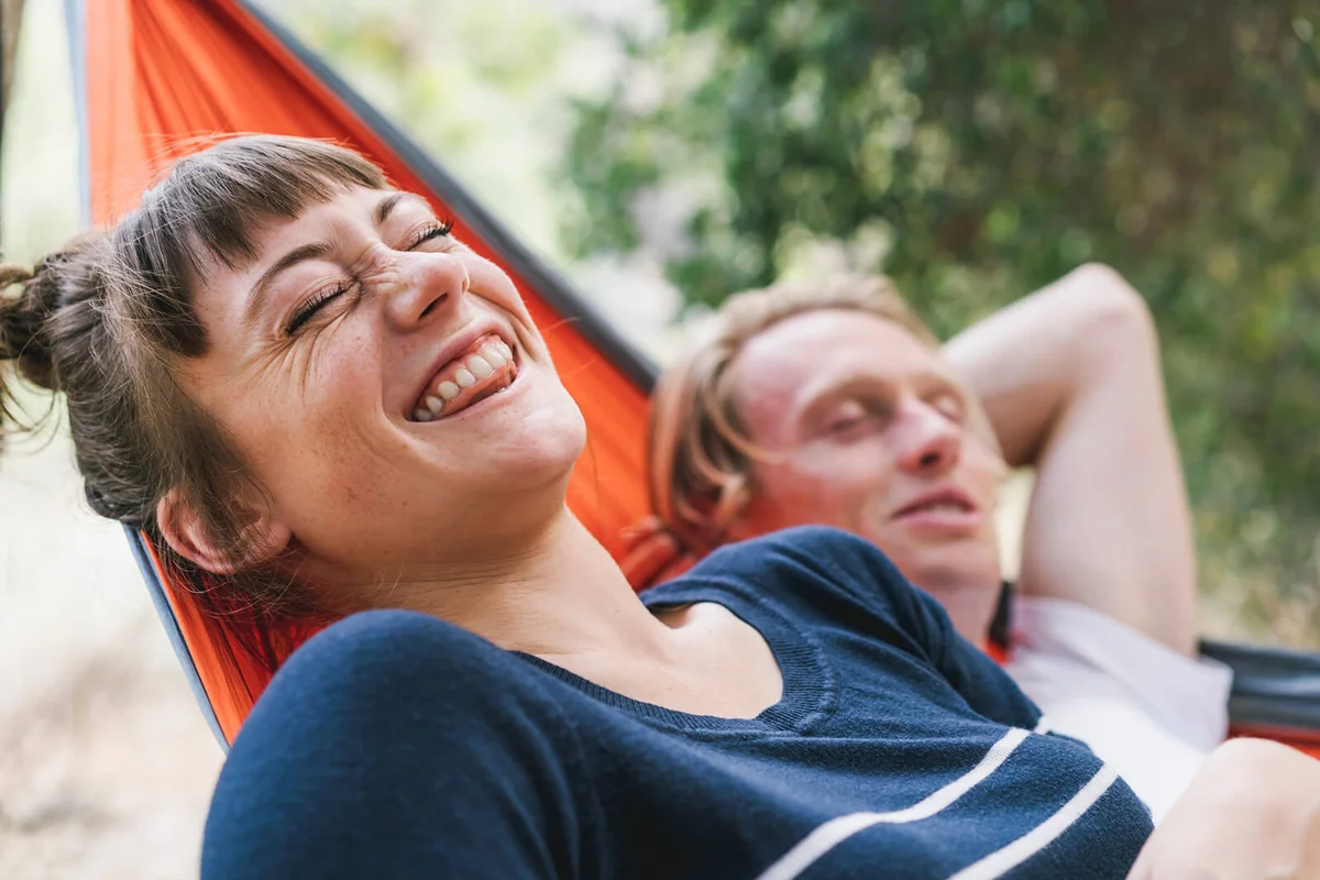 Young woman laughing while lying next to boyfriend in hammock