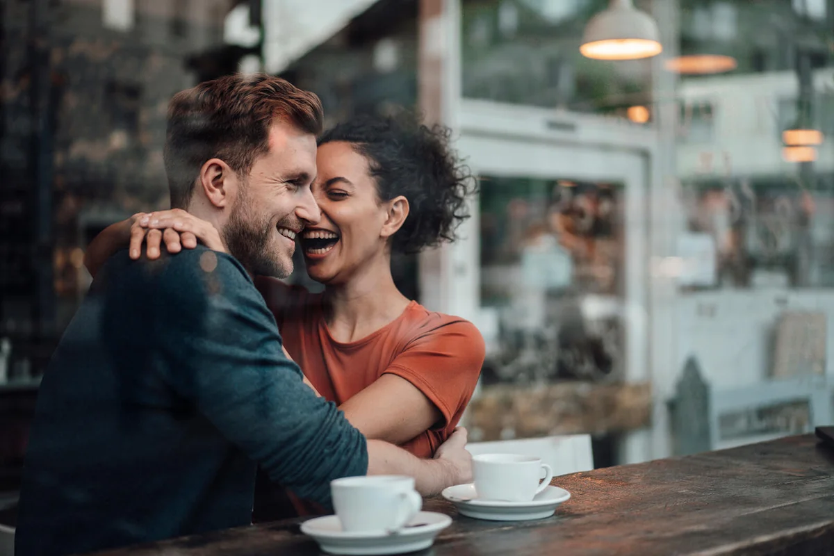 Cheerful woman sitting with arm around on man at cafe