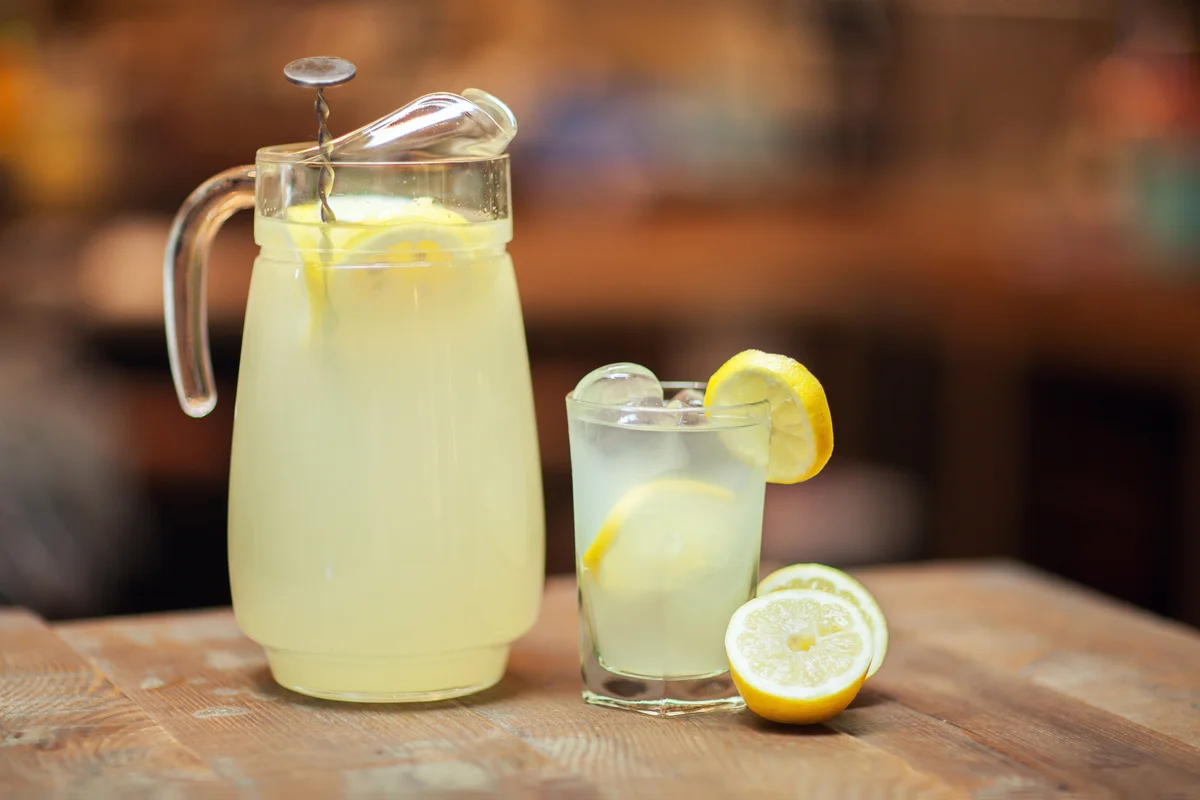 Close view of Glass jar and glass with fresh lemonade on wooden table. Lemon slices.