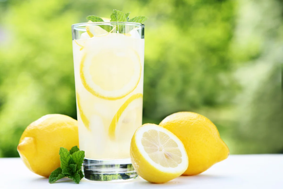 Lemonade garnished with lemon and mint in highball glass in outside setting