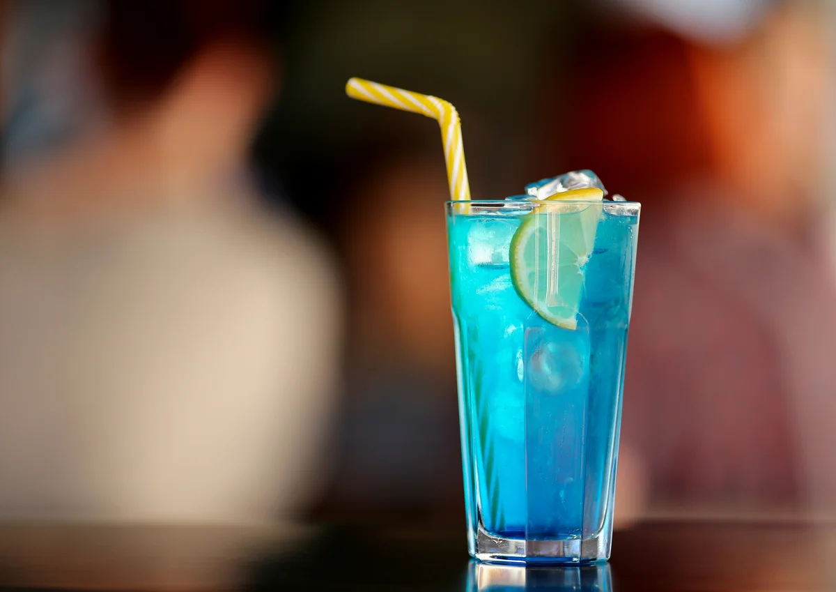 Glass of bright blue electric lemonade cocktail garnished with lemon