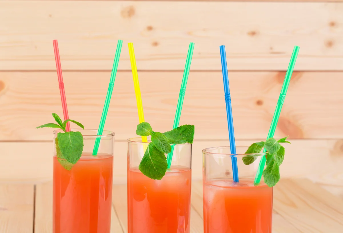 Three glasses of watermelon lemonade with colorful drinking straws and mint garnish