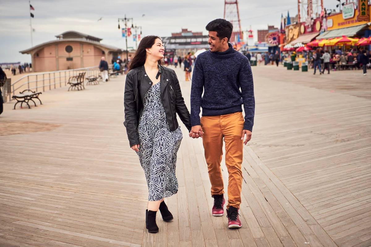 Couple holding hands walking along amusement park boardwalk