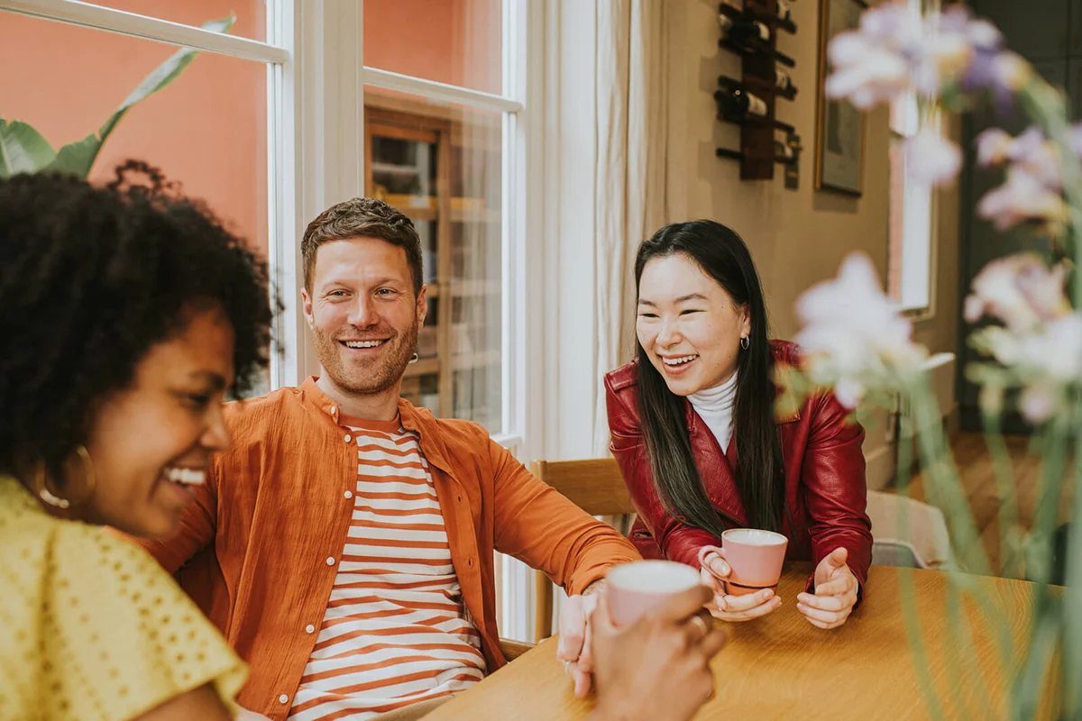 Three young people sit around a table and giggle