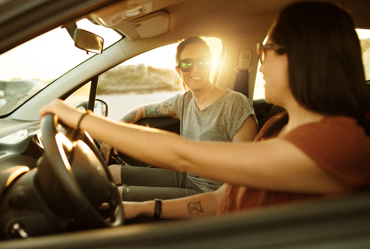Two young women smiling and having fun in the car with the sun shining in behind