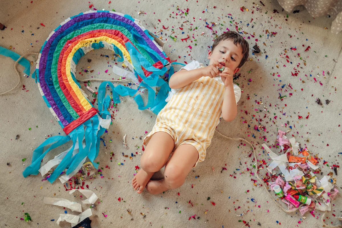 Boy laying next to rainbow pinata and rainbow confetti