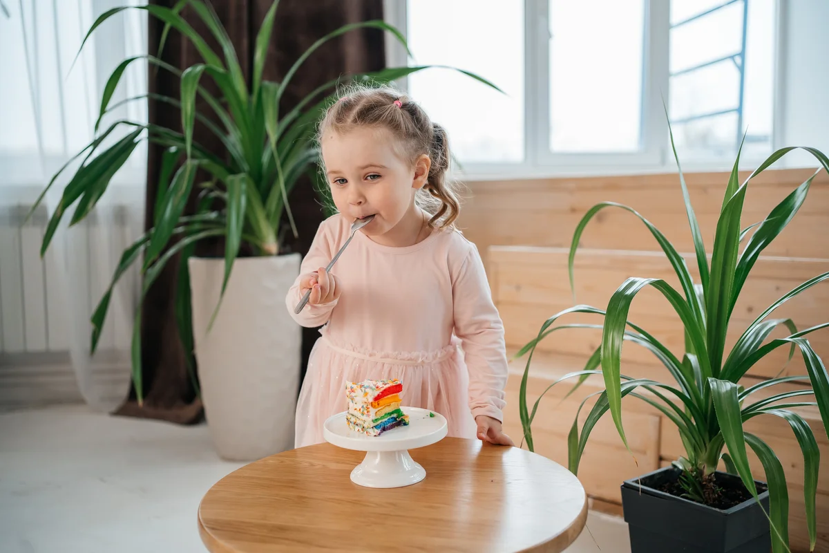 Little girl eating a slice of rainbow cake