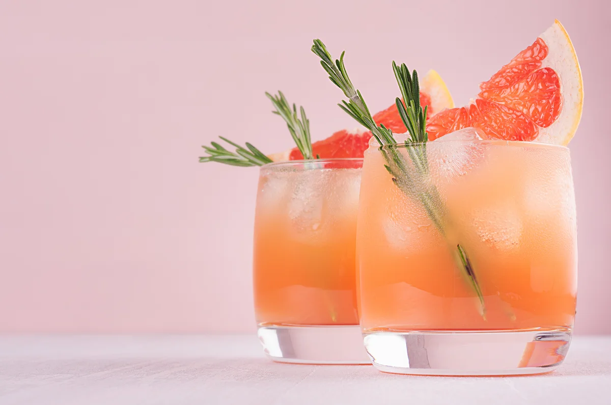 Two glasses with pink beverage, garnished with rosemary and grapefruit