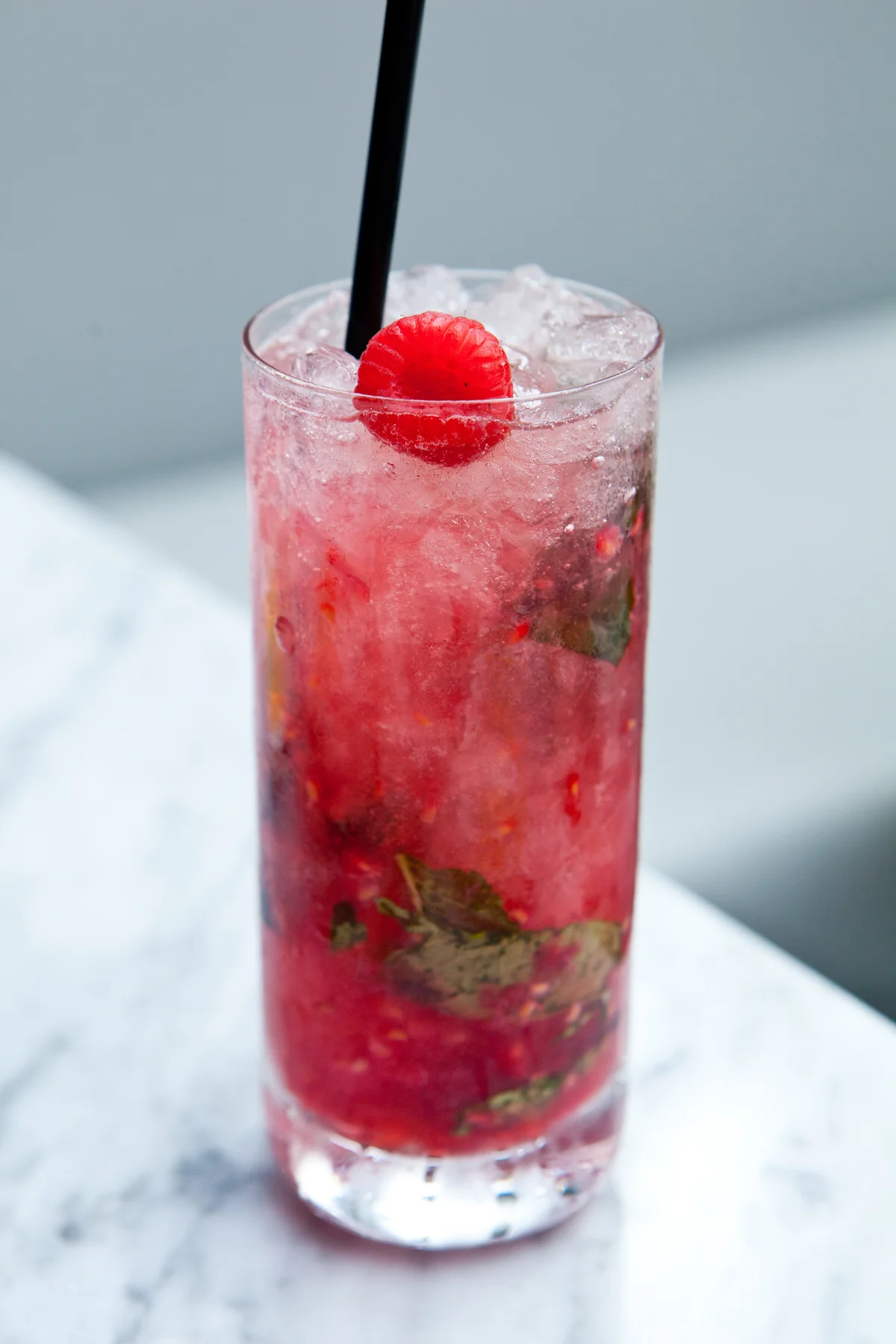 Cocktail with crushed ice and raspberry garnish in highball glass