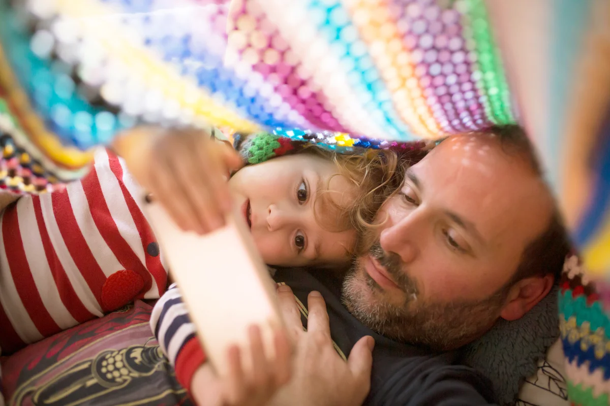 Boy and uncle watching something in a smartphone under a colorful blanket