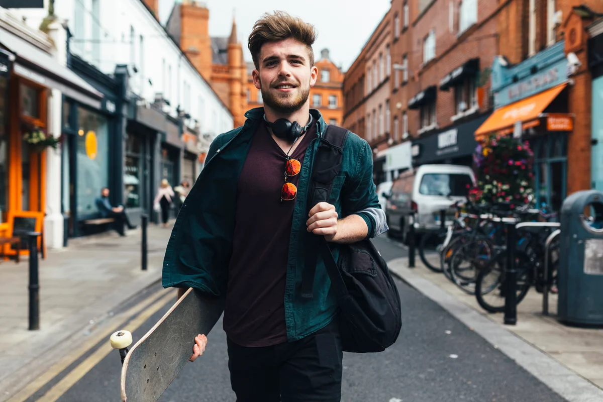 portrait of young man with skateboard walking on the street