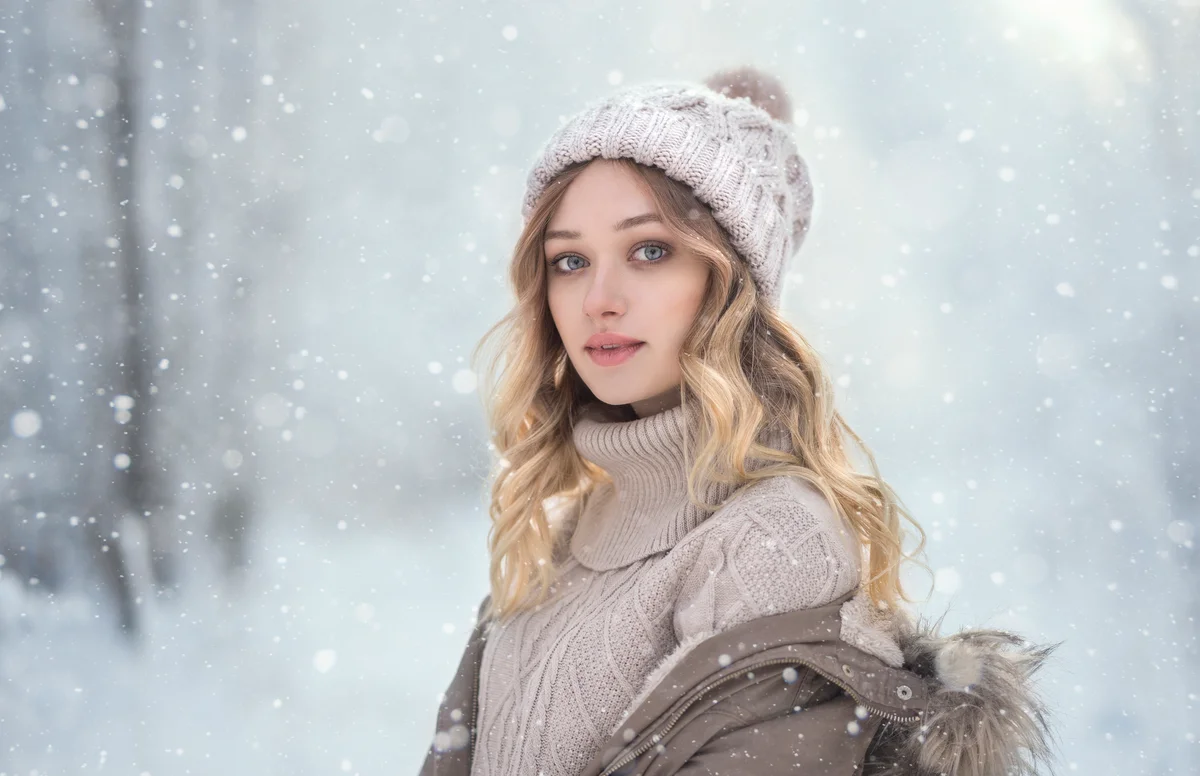 Portrait of young woman in woolly hat under snowfall