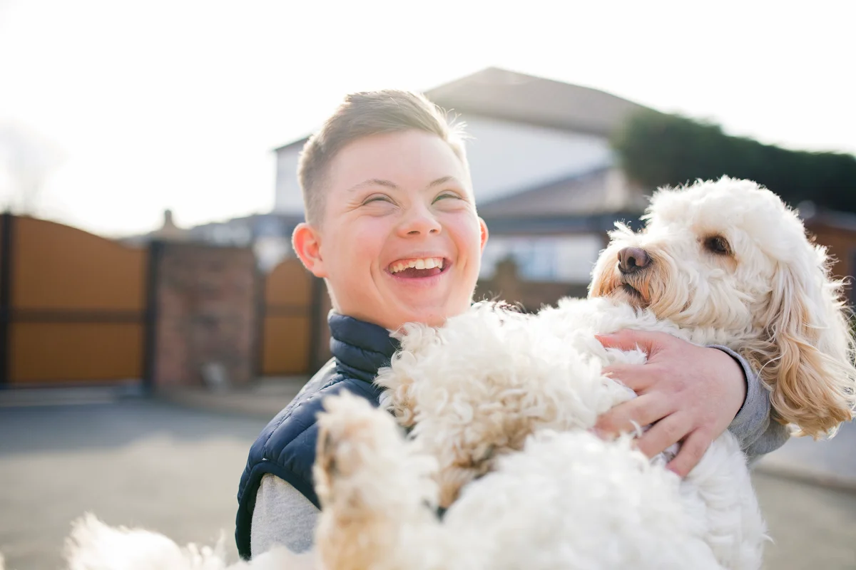 Teen with down syndrome holding white dog and smiling