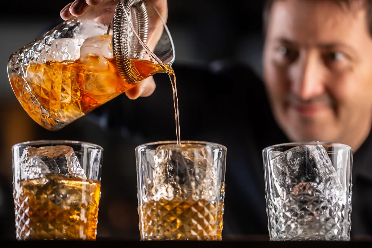 Whisky bourbon on ice being prepared by a professional bartender pouting the drink into ornamental glasses