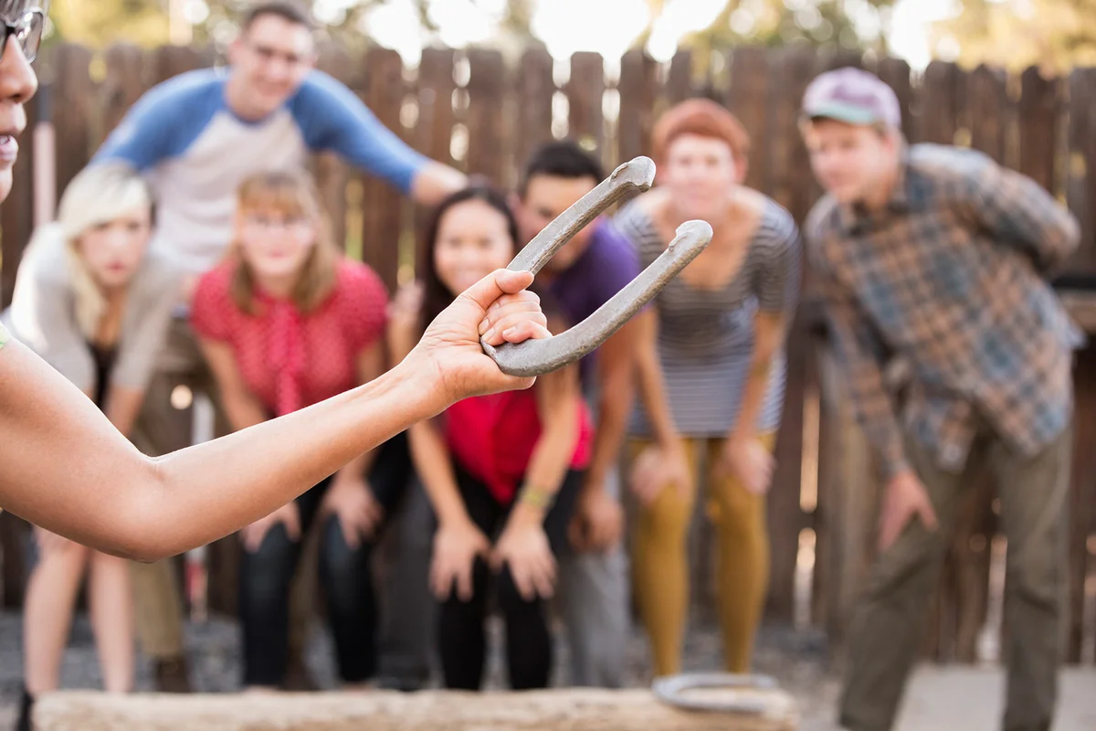 Friends watching woman play horseshoe in backyard