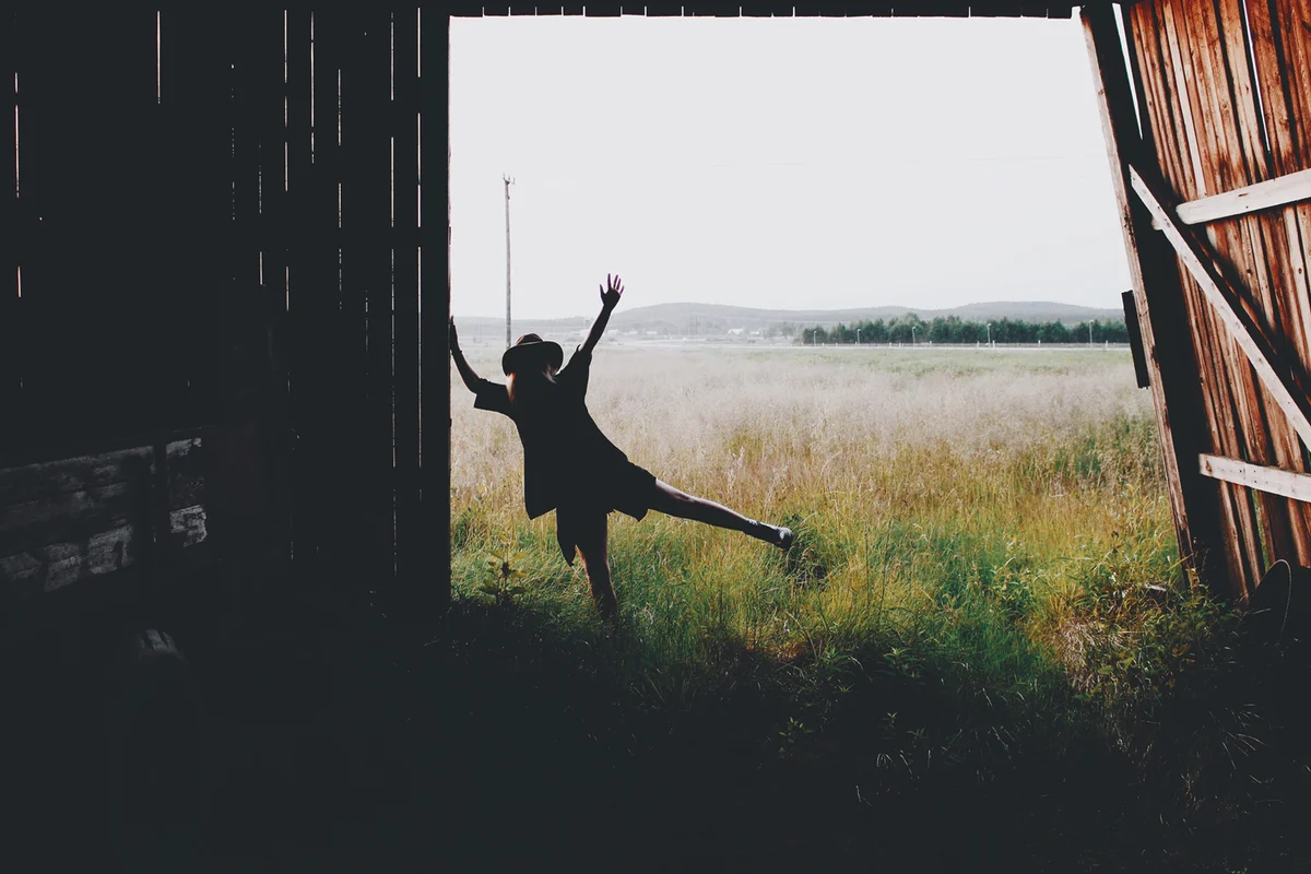 Rear View Of Woman Dancing On Grassy Field At Barn Entrance