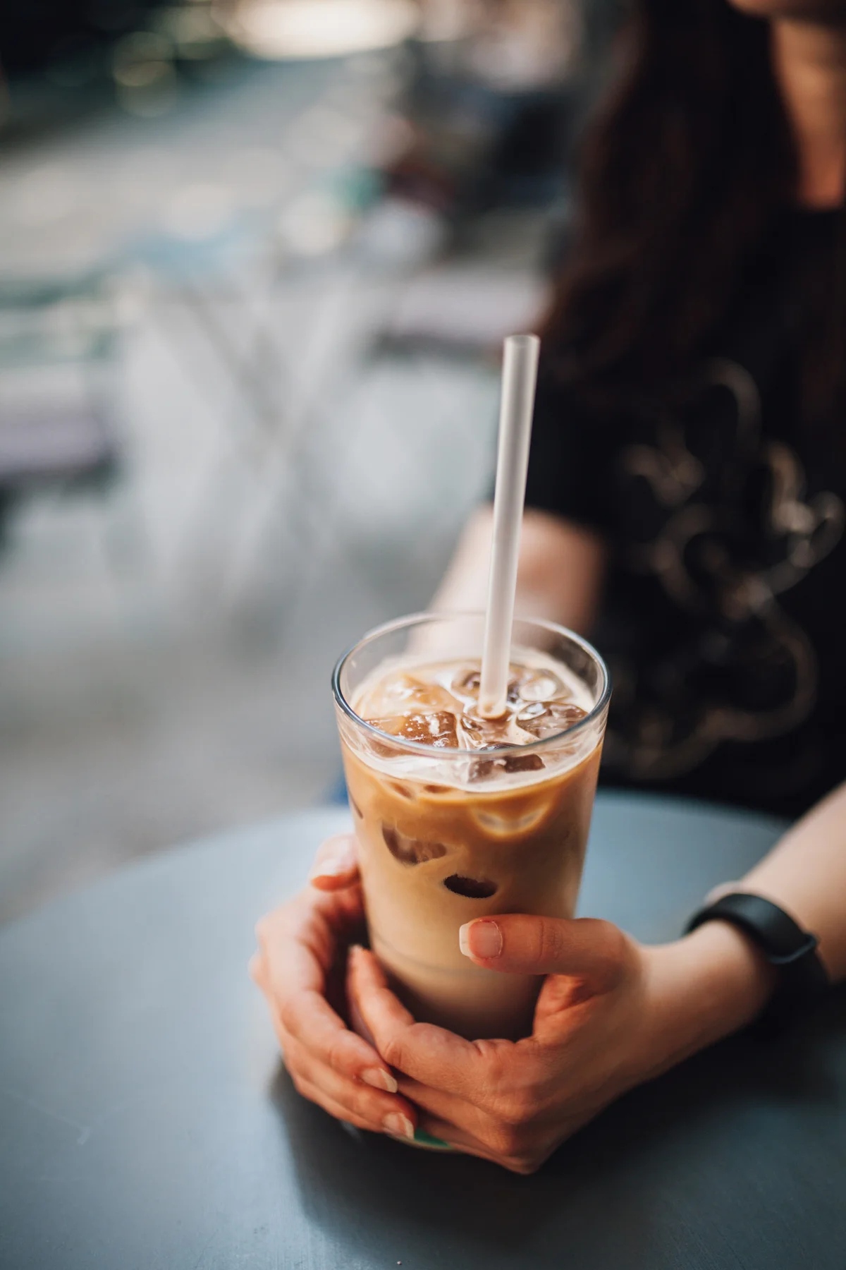 Woman holding large iced creamy coffee in glass with straw
