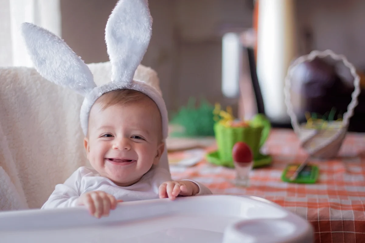 smiling baby with bunny ears in highchair