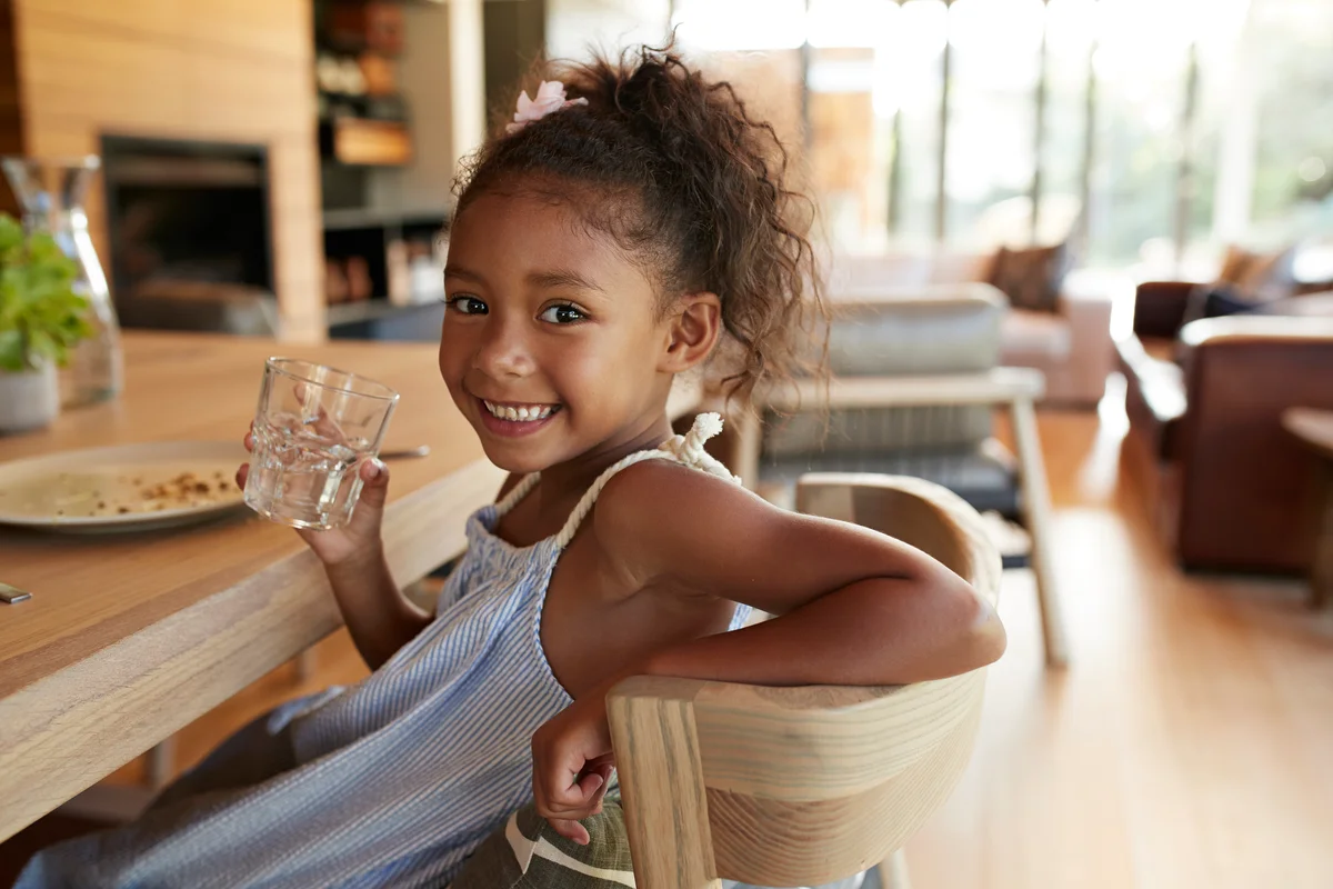 Girl sitting at dinner table with glass of water, smiling at camera