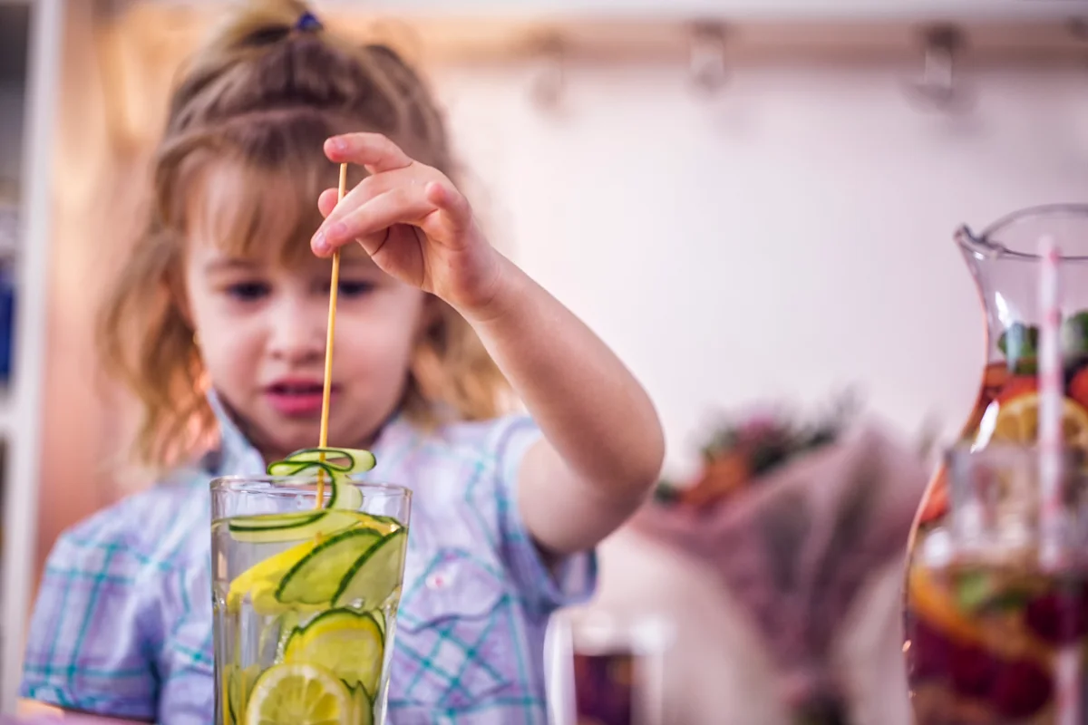 Little girl drinking water infused with lemon & cucumber