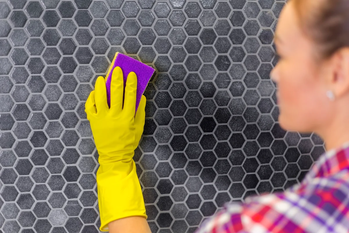woman scrubbing shower tile with sponge