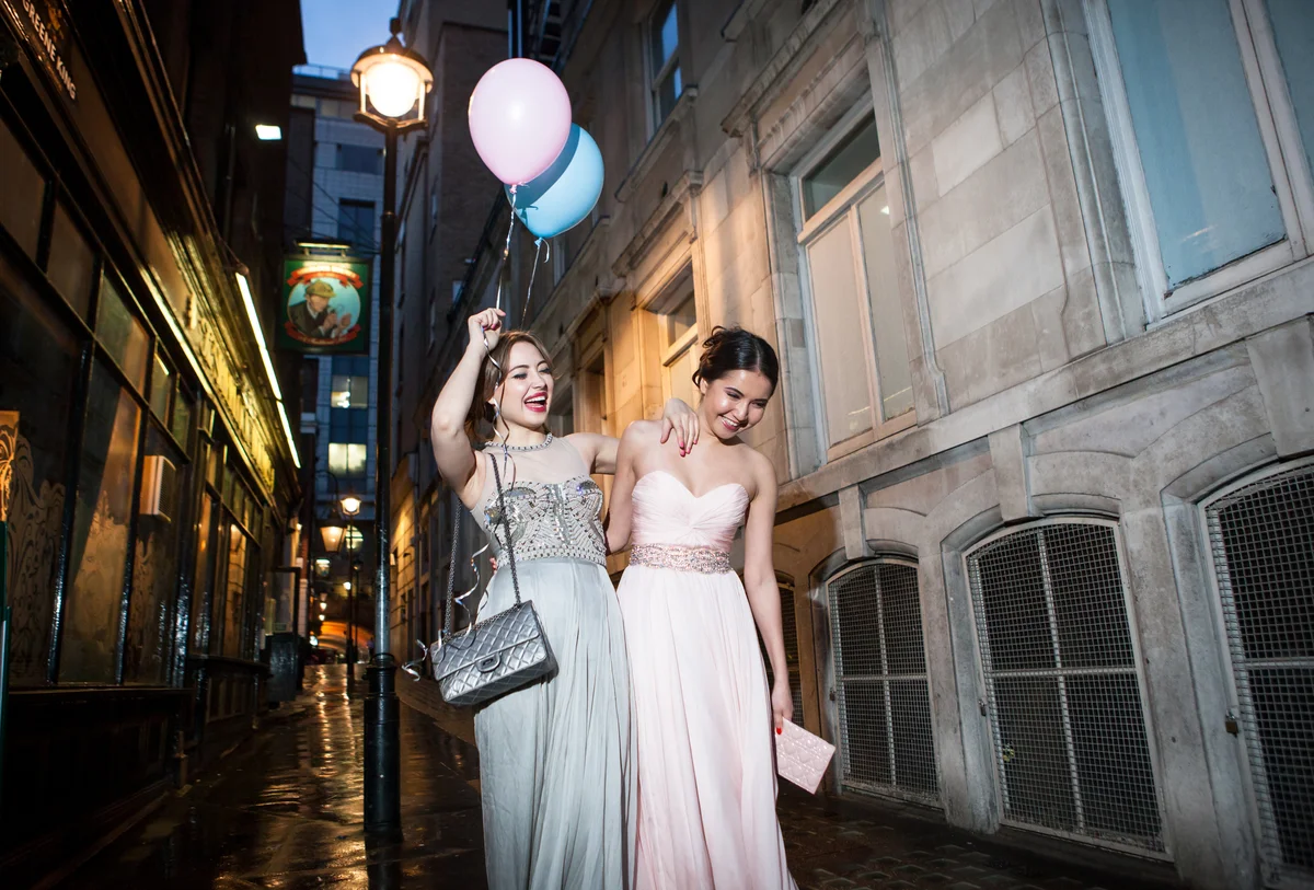 Two friends in prom dresses taking picture in front of cool buildings