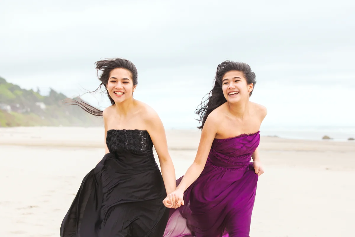 Two girls in evening gowns running barefoot on the beach