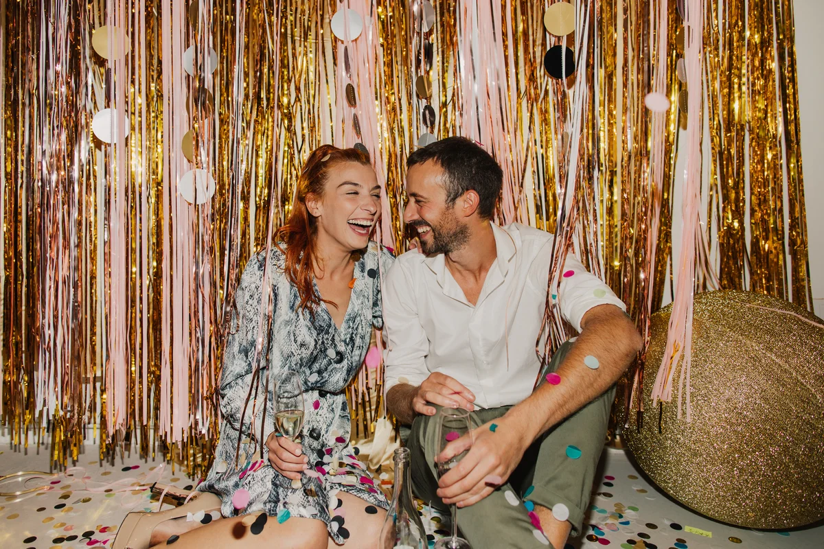 Couple sitting on floor against gold party backdrop