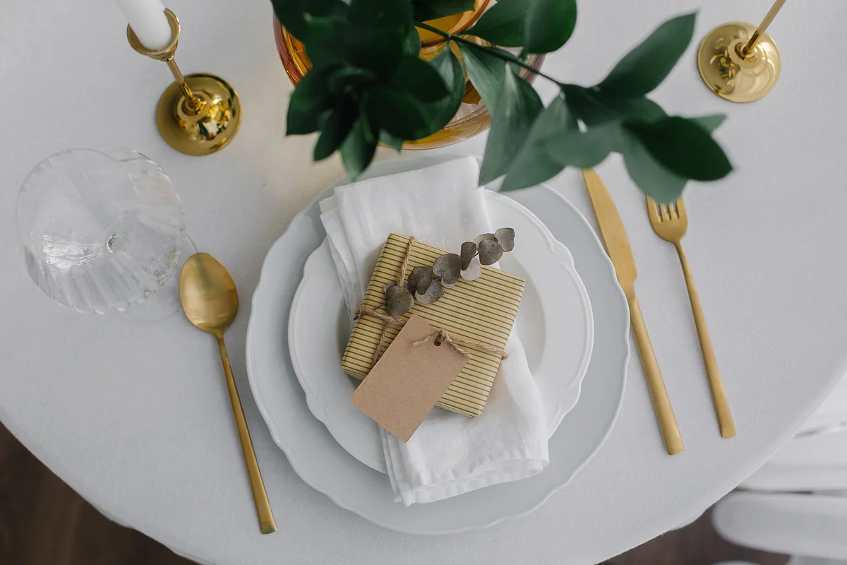 table settings with gold silverware and gold candlesticks and greenery