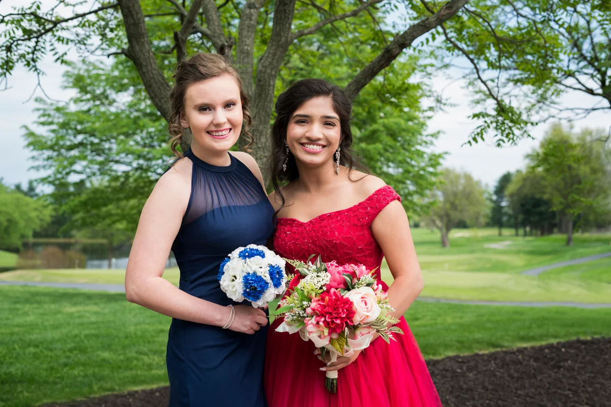 Two best friends at prom, in red and navy dresses.