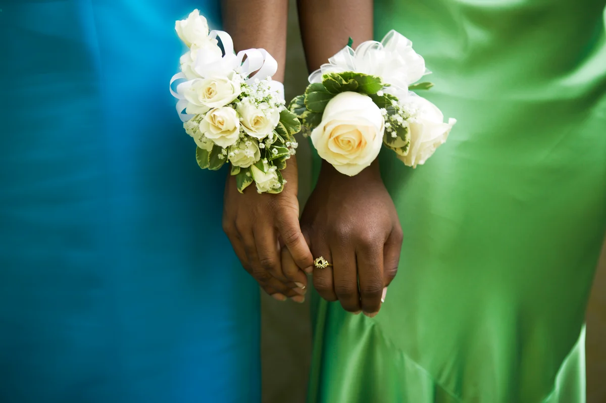 Closeup of corsages on two girls holding hands, wearing green and blue dresses