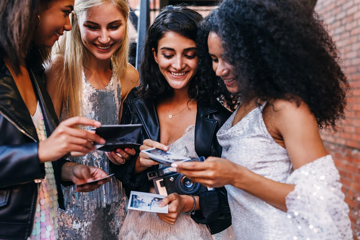 4 friends looking at polaroid photos on prom