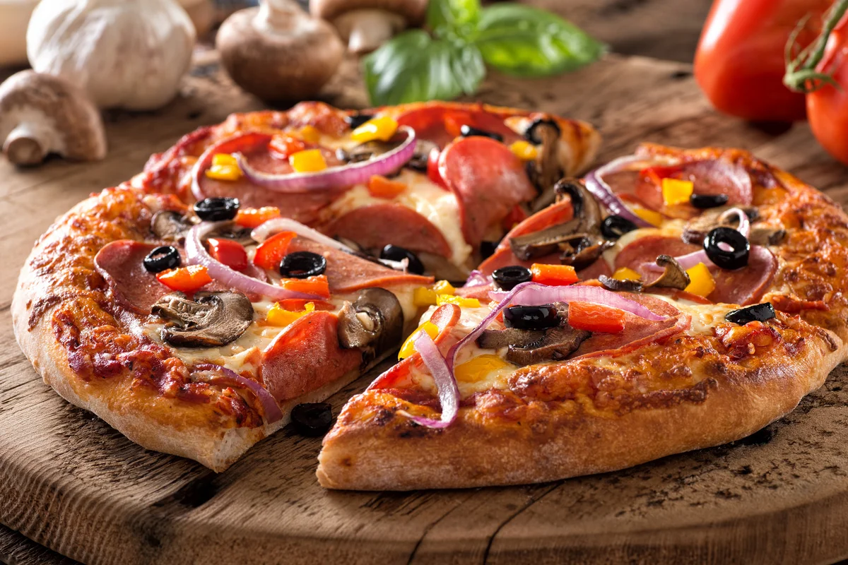 A rustic homemade pepperoni pizza with mushrooms, peppers, red onion and black olives on a rustic board.