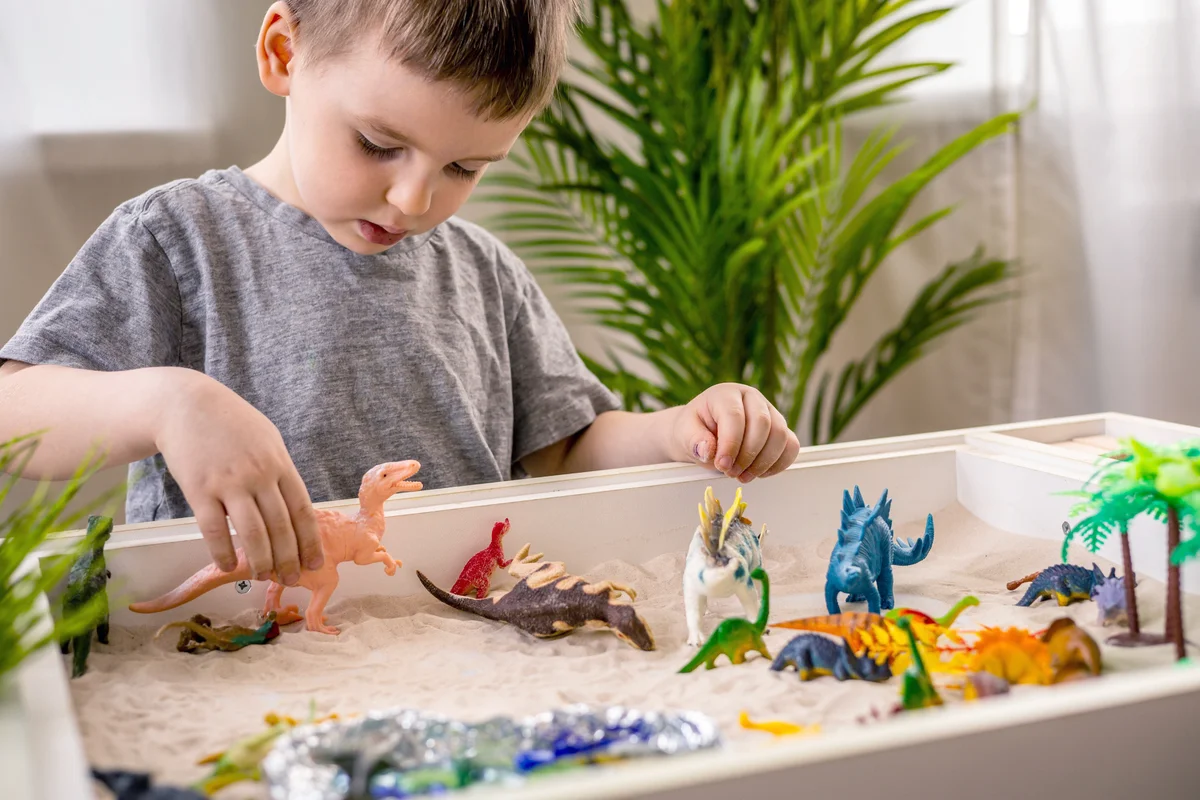 Boy playing with sensory bin with dinosaurs