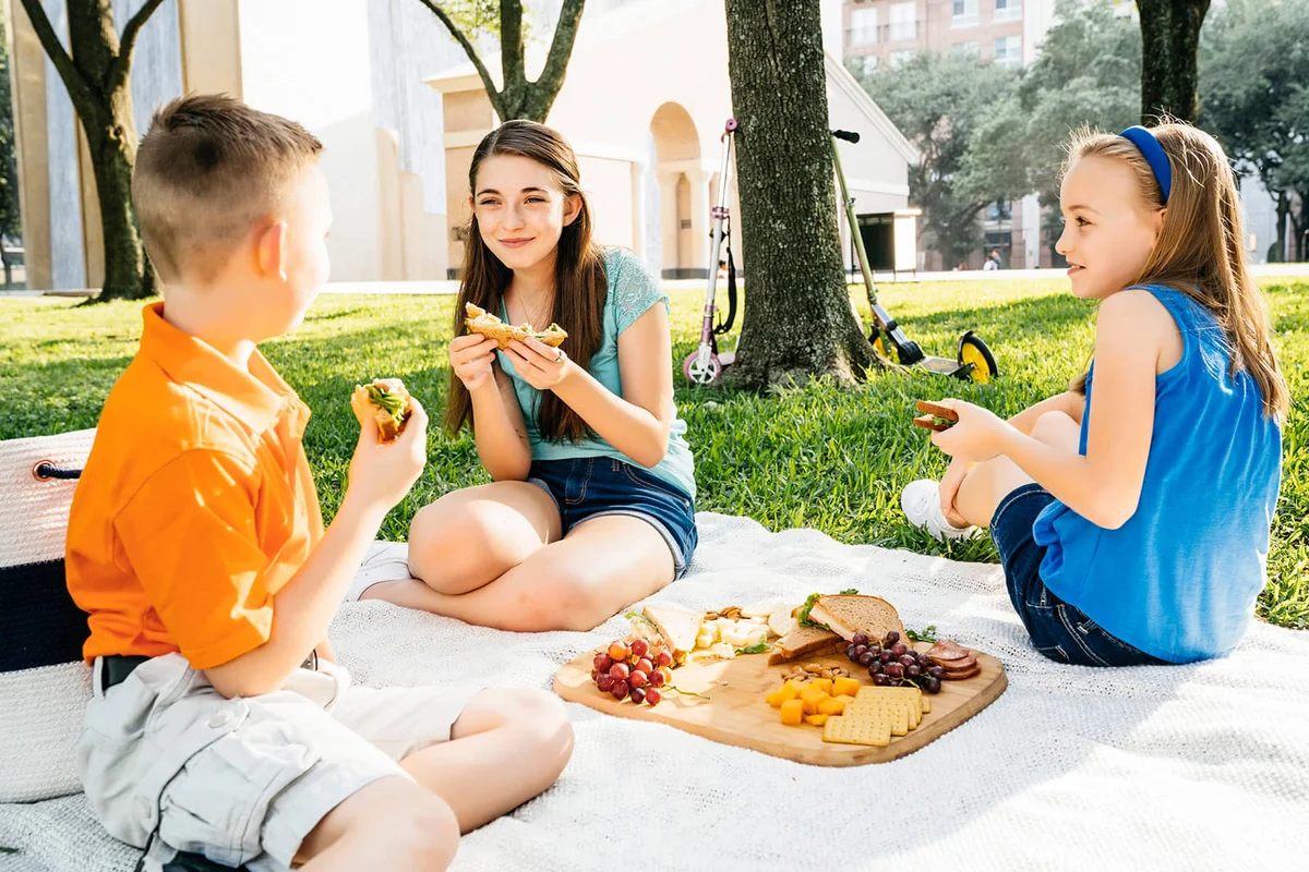 Smiling Caucasian brother and sisters eating food at picnic