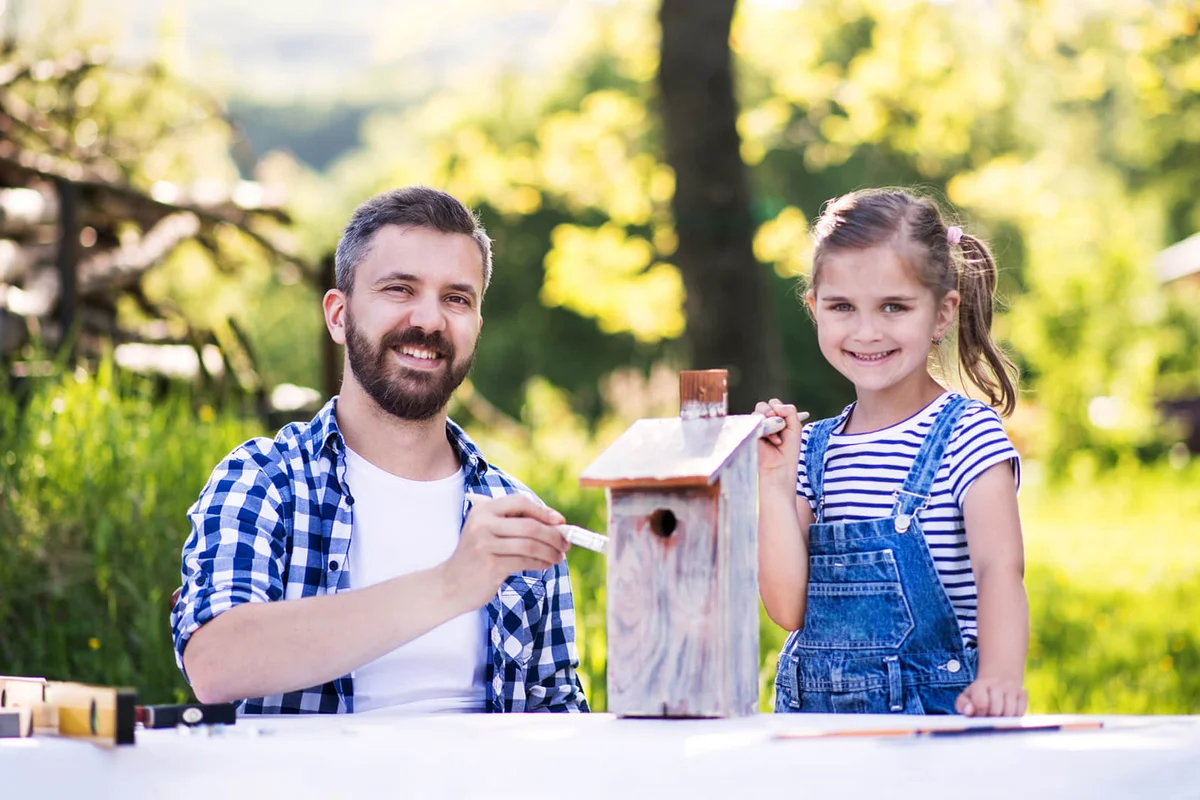 Father With A Small Daughter Outside, Painting Wooden Birdhouse