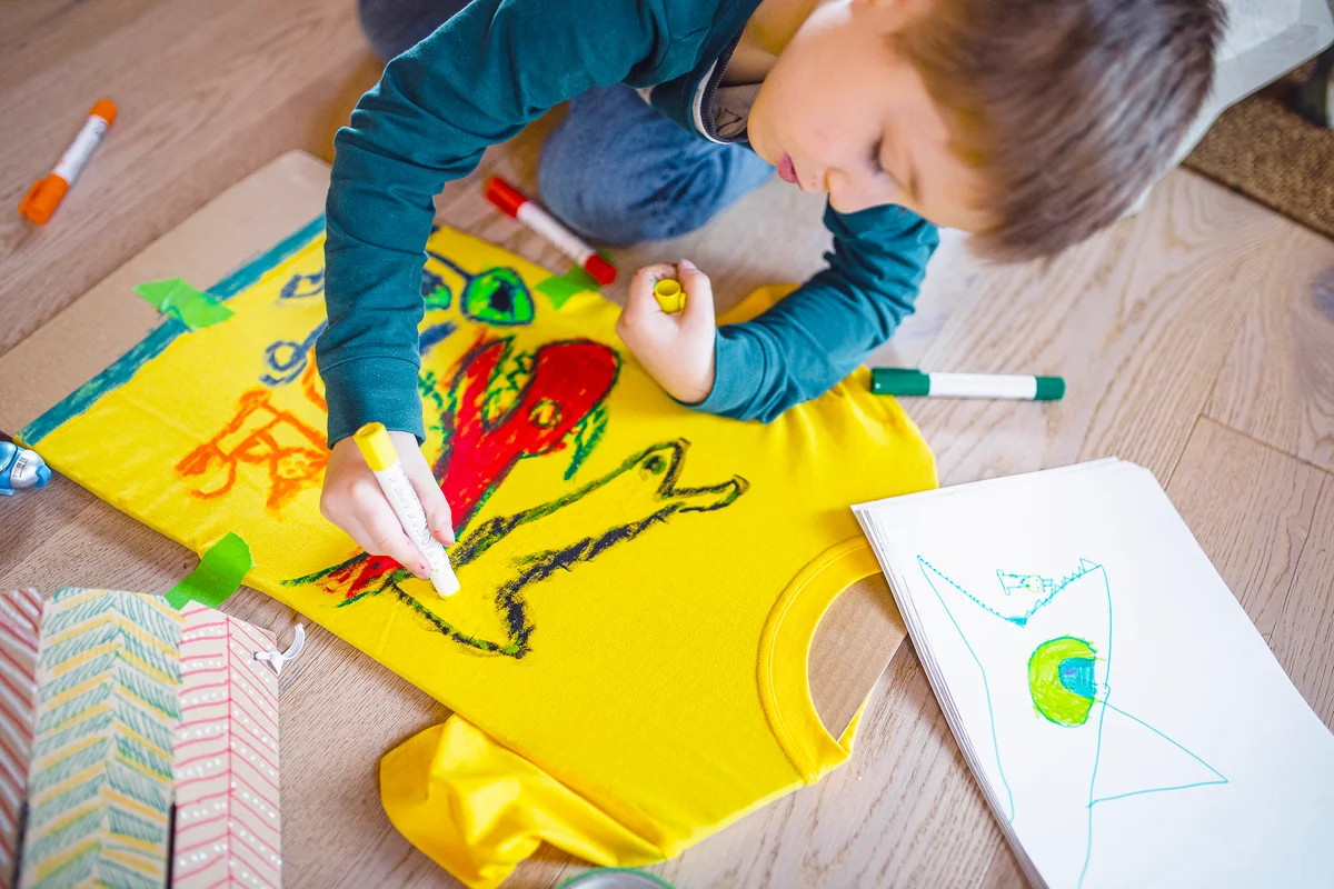 Young child drawing his own artwork on shirt at home