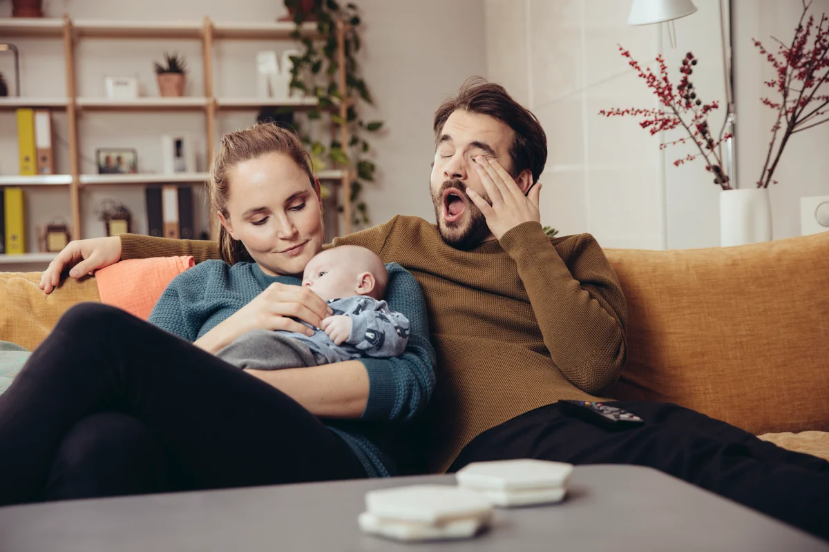 Mom and dad cuddling baby while dad yawns