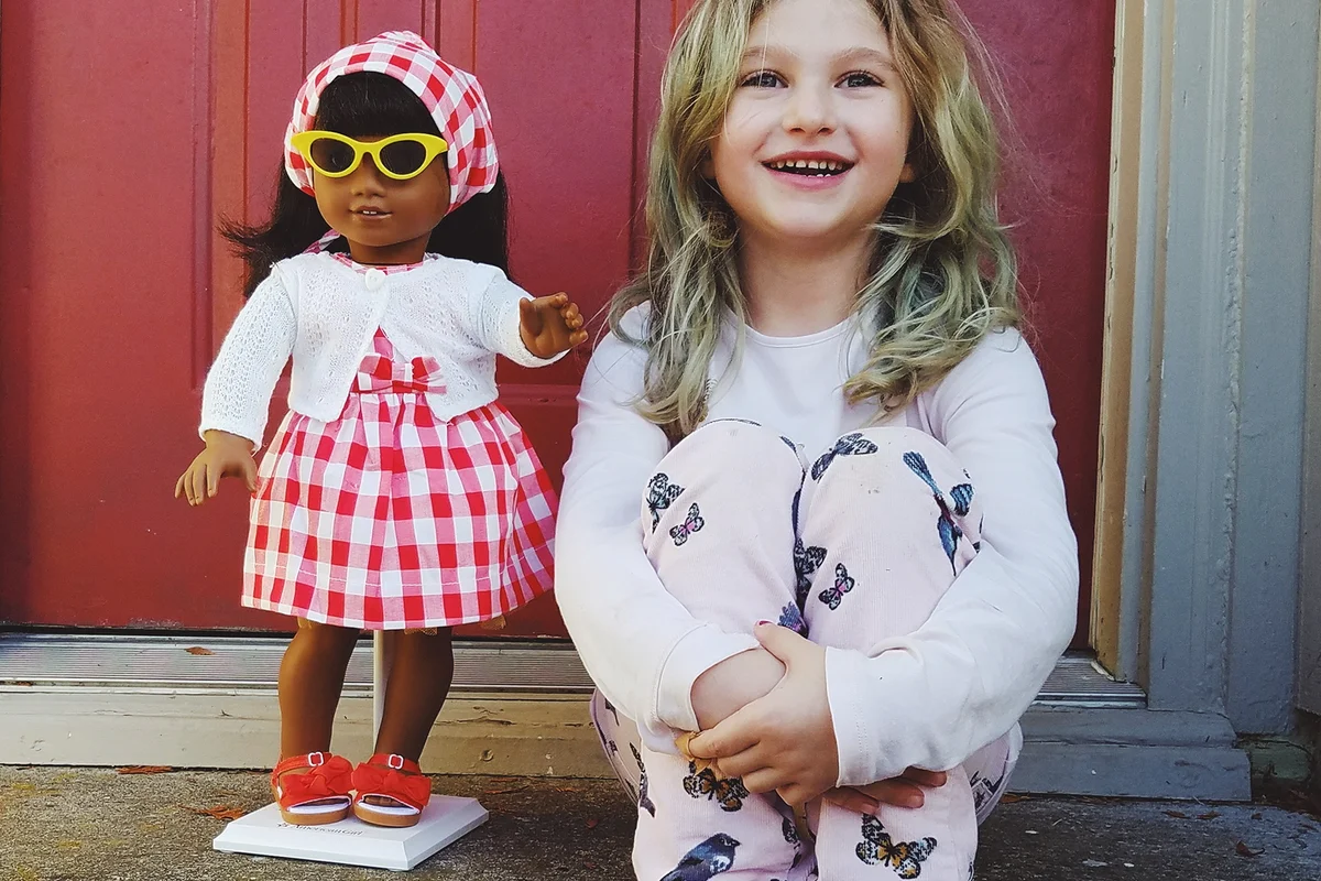 Smiling Girl Standing Against Wall With American Girl Doll
