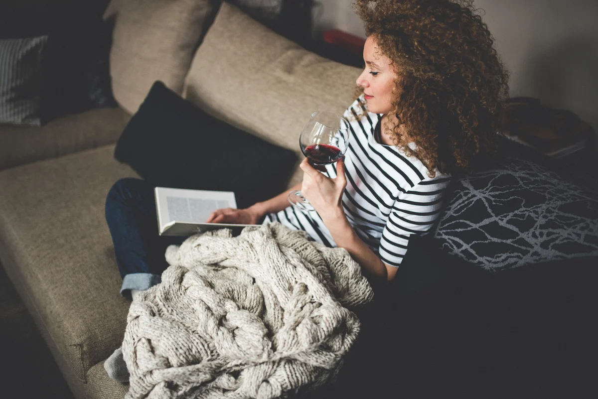 woman reading book and drinking glass of wine