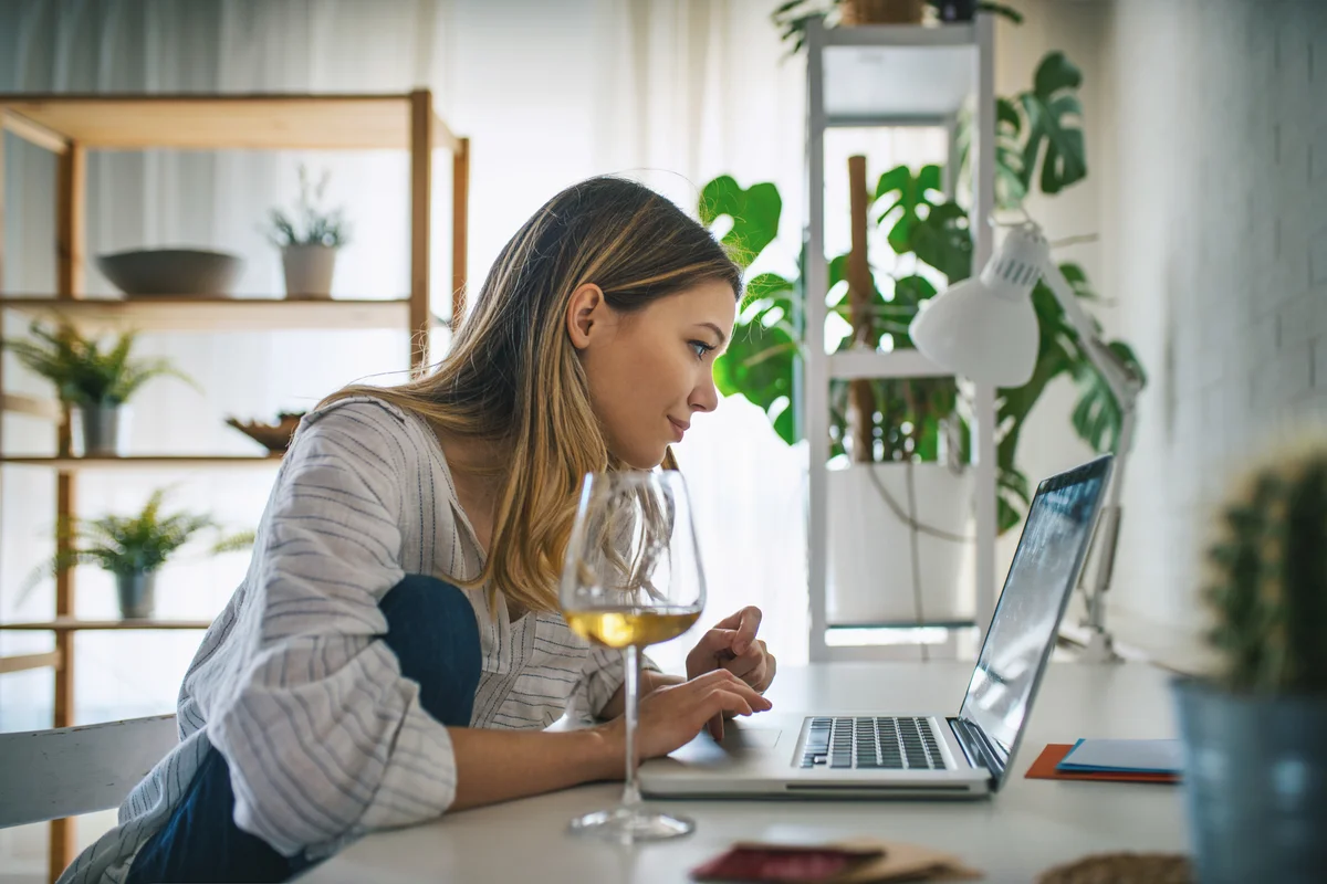 Young woman working on laptop with glass of wine