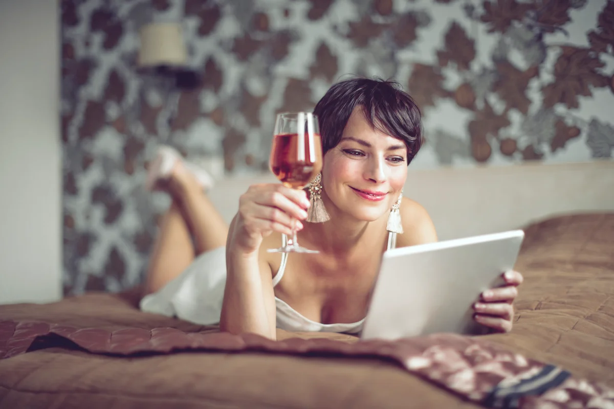Woman enjoying glass of rose wine on bed