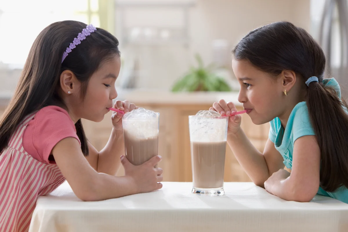 two girls blowing bubbles in chocolate milk