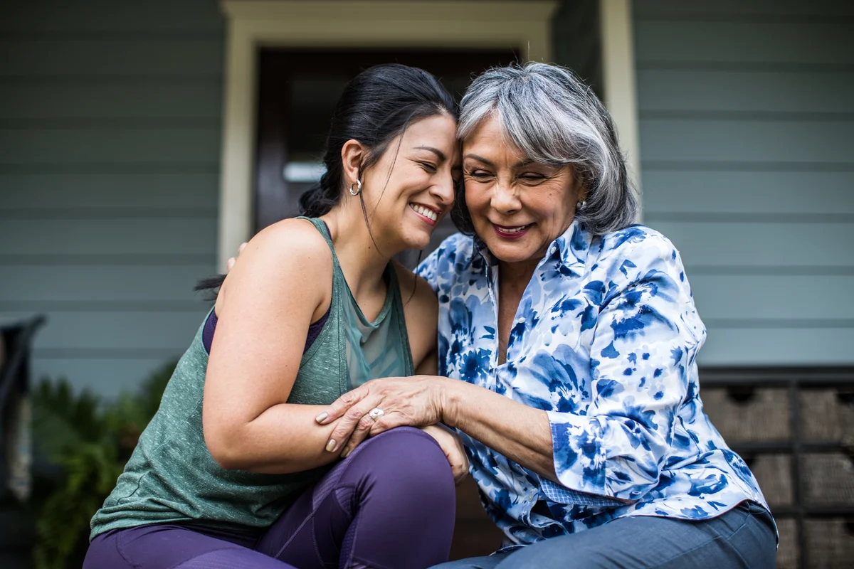 Senior woman and adult daughter hugging and  laughing on porch