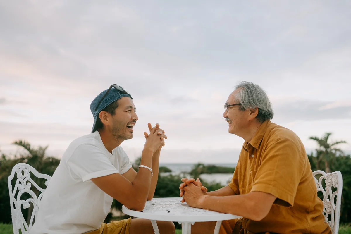 Senior dad and adult son sitting outside on patio and chatting