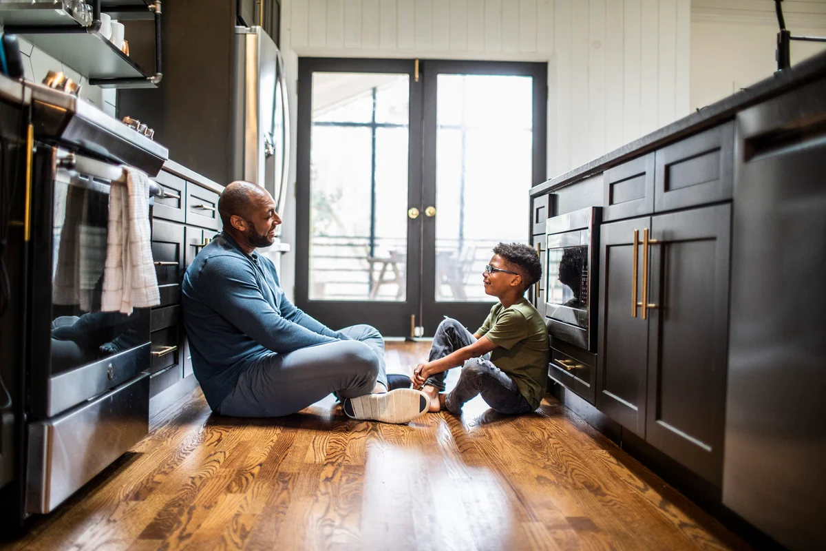 Dad and son sitting on floor in kitchen having conversation