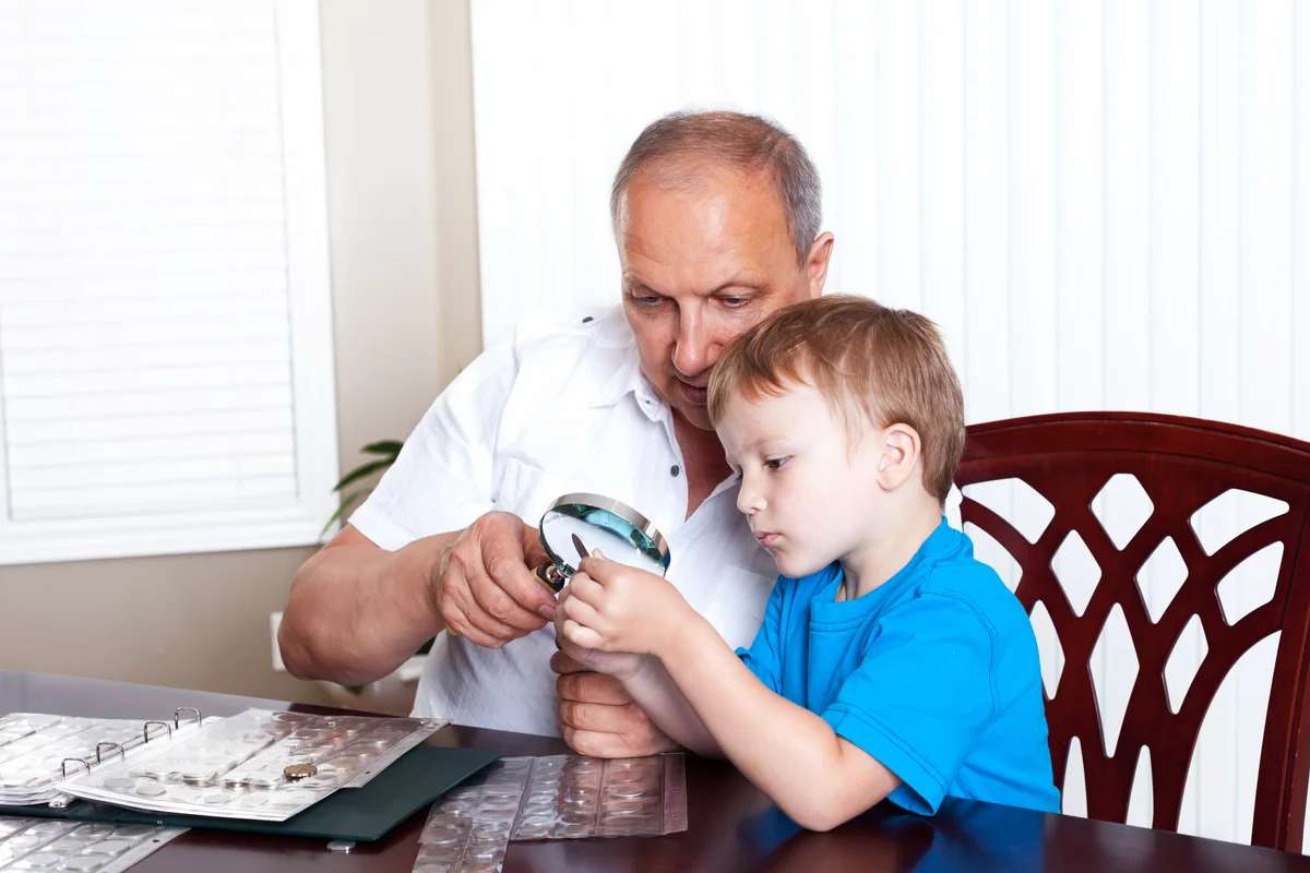 Grandfather and grandson looking closely at coin collection with magnifying glass